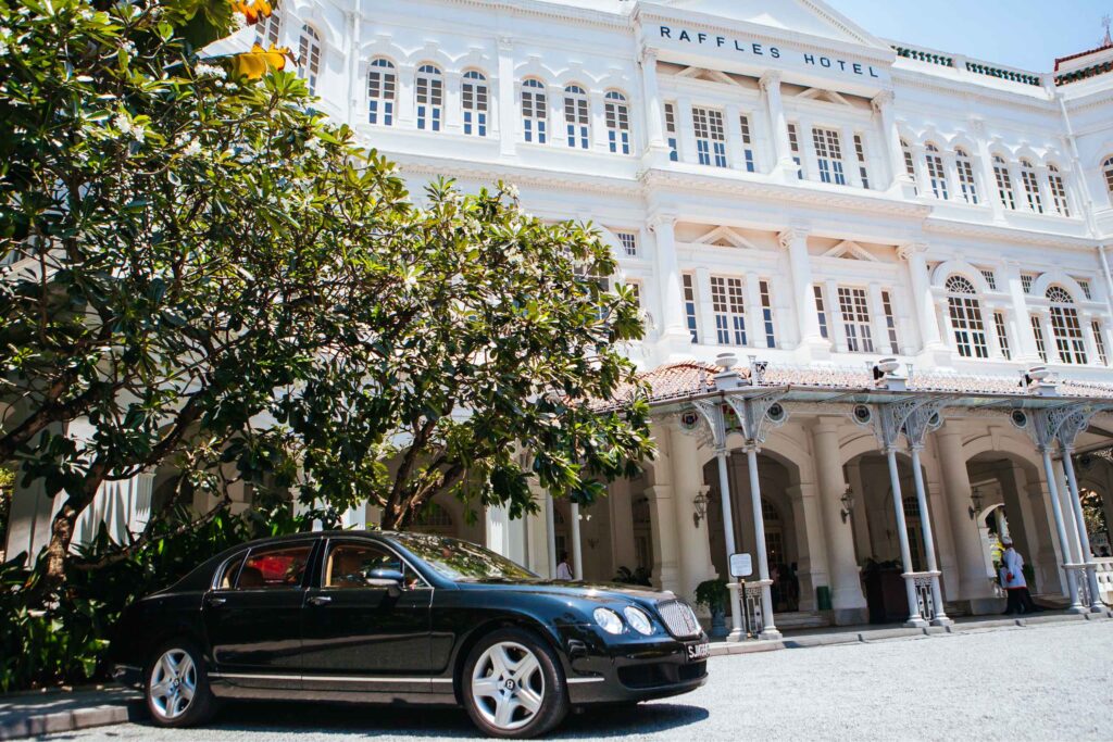 Colonial white facade of Raffles Hotel with black car parked outside Singapore