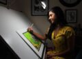 A Singapore illustrator works at her table during the illustration arts fest, surrounded by hand-drawn prints on display