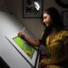 artist-drawing-table-exhibition-unsplash - SINwebzine A Singapore illustrator works at her table during the illustration arts fest, surrounded by hand-drawn prints on display