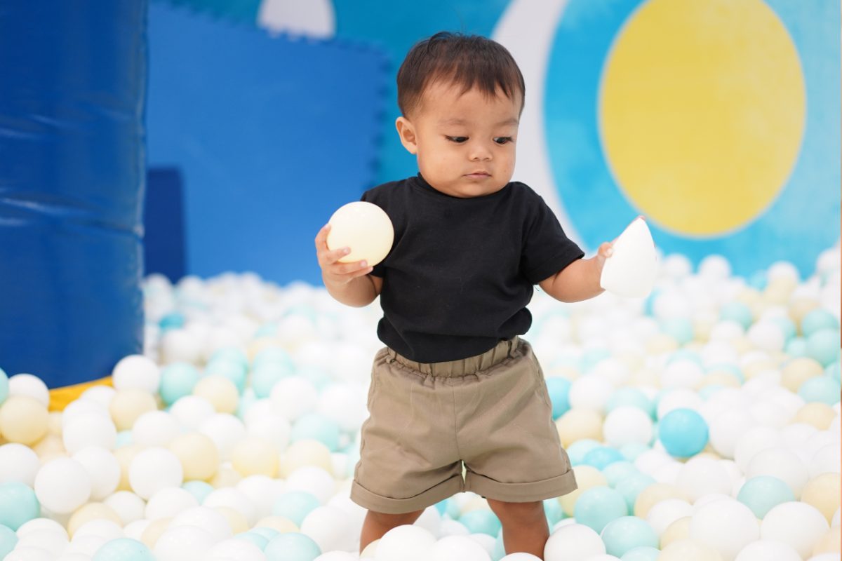 A mother and toddler playing together in a ball pit at an indoor playground, surrounded by bright colours
