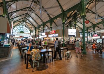 A smiling traveller enjoys a budget getaway meal at a busy Singapore hawker centre
