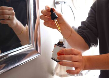 A woman applying anti-frizz serum to damp hair as part of her monsoon beauty routine in a bright bathroom