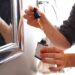 A woman applying anti-frizz serum to damp hair as part of her monsoon beauty routine in a bright bathroom