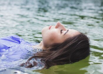 A woman resting peacefully inside a float therapy pod in a Singapore wellness studio, eyes closed in deep relaxation.