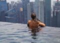 A woman relaxing by an infinity pool during a luxury staycation in Singapore with the city skyline in the background