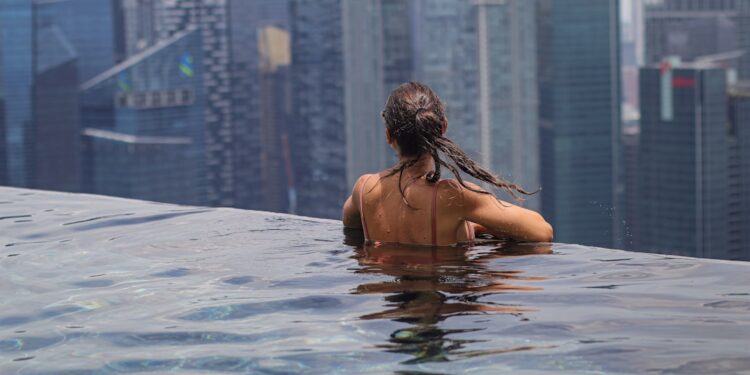 A woman relaxing by an infinity pool during a luxury staycation in Singapore with the city skyline in the background