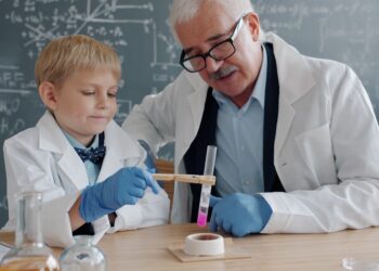 A child conducting hands-on science workshops at a classroom table wearing safety goggles and mixing colourful liquids.