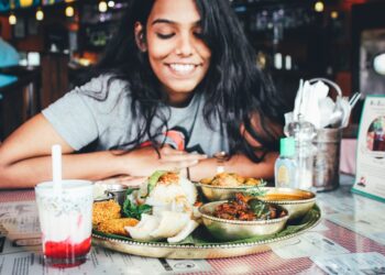A Singaporean expat woman shares a meal at an outdoor hawker-style food stall, connecting community through food abroad