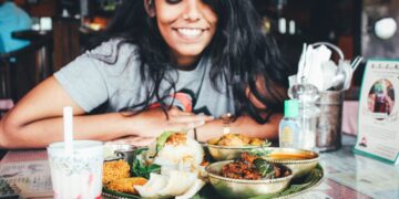 singaporean-woman-eating-hawker-food-unsplash - SINwebzine A Singaporean expat woman shares a meal at an outdoor hawker-style food stall, connecting community through food abroad