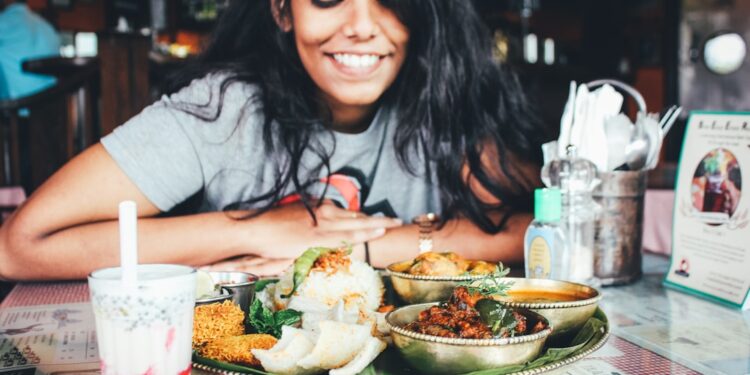 singaporean-woman-eating-hawker-food-unsplash - SINwebzine A Singaporean expat woman shares a meal at an outdoor hawker-style food stall, connecting community through food abroad