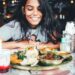 singaporean-woman-eating-hawker-food-unsplash - SINwebzine A Singaporean expat woman shares a meal at an outdoor hawker-style food stall, connecting community through food abroad