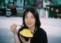 woman-eating-soup-street-food-unsplash - SINwebzine A woman enjoying a bowl of laksa at a busy Singapore hawker centre stall