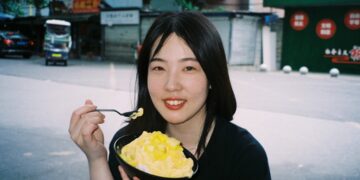 woman-eating-soup-street-food-unsplash - SINwebzine A woman enjoying a bowl of laksa at a busy Singapore hawker centre stall