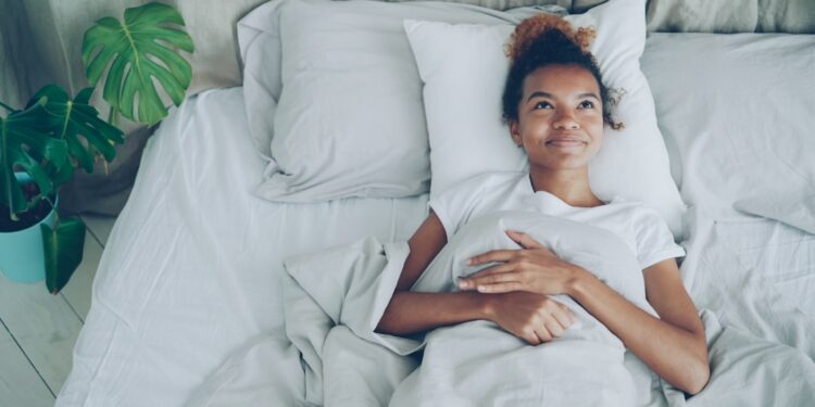 A woman lying awake in a warm Singapore bedroom, struggling with July humidity and poor sleep
