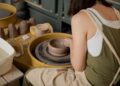 A woman shapes clay at a pottery wheel inside one of Singapore's ceramic studios, focused and hands covered in clay