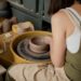 A woman shapes clay at a pottery wheel inside one of Singapore's ceramic studios, focused and hands covered in clay