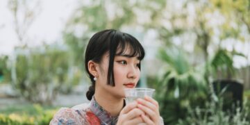 asian-woman-drinking-water-morning-unsplash - SINwebzine A professional woman beginning her morning routine in Singapore by drinking water at sunrise before the heat builds