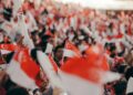 A crowd of Singaporeans cheering together inside a stadium during the National Day Parade, dressed in red and white
