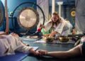 woman-lying-down-singing-bowl-session-unsplash - SINwebzine A woman resting during a sound bath session in a Singapore wellness studio, surrounded by singing bowls and soft light.