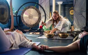 A woman resting during a sound bath session in a Singapore wellness studio, surrounded by singing bowls and soft light.