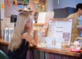 woman-reading-restaurant-menu-unsplash - SINwebzine A woman carefully reviews a buffet menu at a Singapore National Day celebration, making informed gluten-free choices