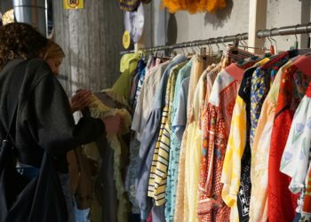 A woman carefully browsing a clothing rack at one of Singapore's secondhand platforms, looking for preloved fashion finds.