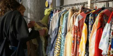 woman-browsing-clothing-rack-thrift-store-unsplash - SINwebzine A woman carefully browsing a clothing rack at one of Singapore's secondhand platforms, looking for preloved fashion finds.