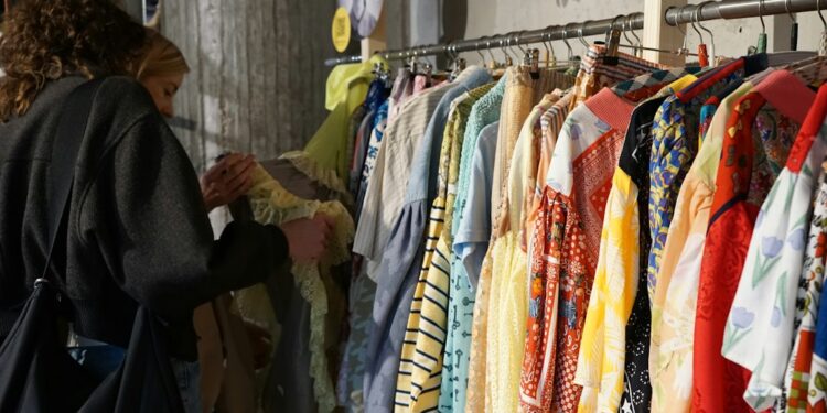 woman-browsing-clothing-rack-thrift-store-unsplash - SINwebzine A woman carefully browsing a clothing rack at one of Singapore's secondhand platforms, looking for preloved fashion finds.