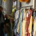 woman-browsing-clothing-rack-thrift-store-unsplash - SINwebzine A woman carefully browsing a clothing rack at one of Singapore's secondhand platforms, looking for preloved fashion finds.