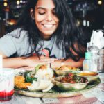 Una mujer expatriada singapurense comparte una comida en un puesto de comida al aire libre estilo hawker, conectando a la comunidad a través de la comida en el extranjero.