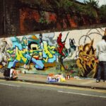 Un joven pintando un gran mural de arte callejero en una pared exterior durante un programa juvenil de Singapur