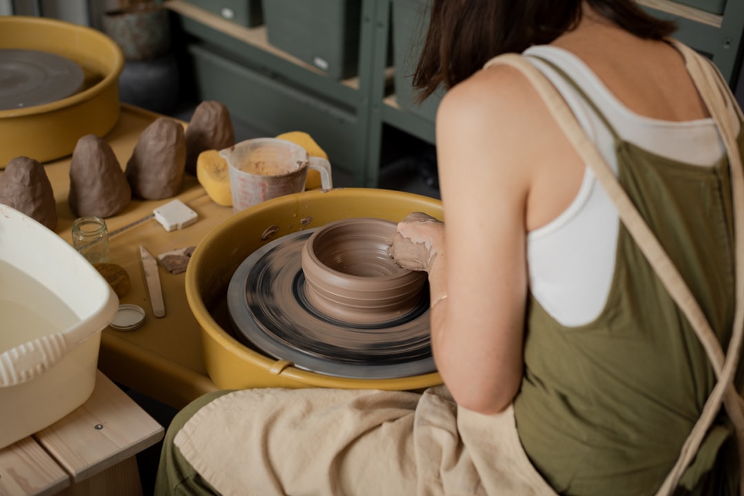A woman shapes clay at a pottery wheel inside one of Singapore's ceramic studios, focused and hands covered in clay